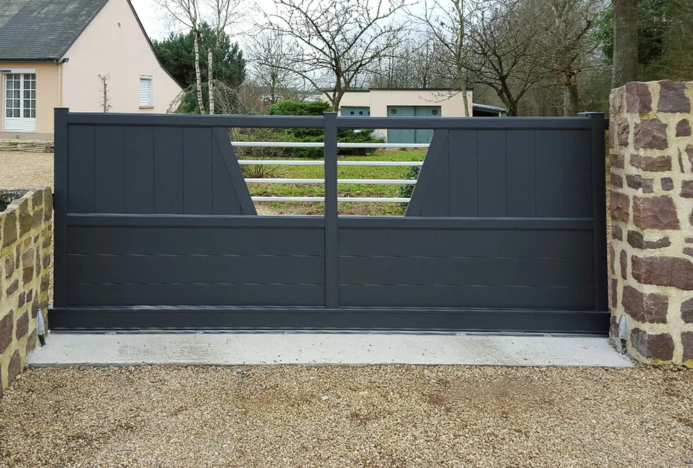 Portail coulissant moderne en aluminium anthracite installé entre piliers en pierre naturelle sur allée gravillonnée
